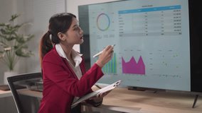 Businesswoman in a red blazer is analyzing financial data displayed on a tv screen, taking notes on a clipboard - Powered by Shutterstock - Get 15% off with code: PIKWIZARD15