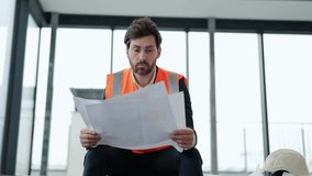 Frustrated architect sits on the floor in modern office building with blueprints. He's wearing suit and orange vest. He's unsure about something. - Powered by Shutterstock - Get 15% off with code: PIKWIZARD15