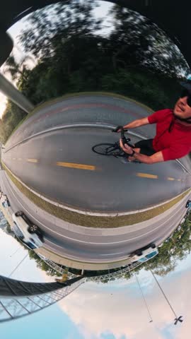 Hyperlapse of a man cycling in a city along the bicycle path made in a form of a little planet with trees and buildings appearing in the frame