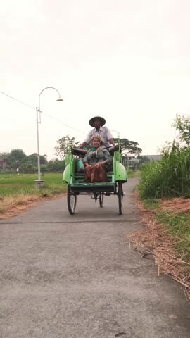 Javanese becak driver pedals down a paved road, transporting a female passenger through a serene countryside setting