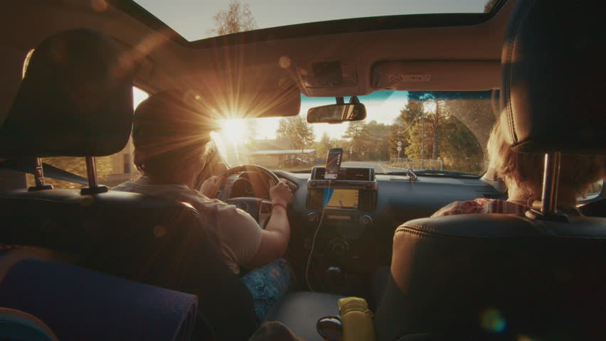 Adult man and elderly woman travel in the car on a rural road during sunset with hiking gear laying inside the car