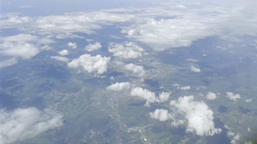 Aerial view from airplane showing Florence Firenze and surrounding Tuscan hills, farmland and scattered clouds under a bright sky, captured during a flight across central Italy