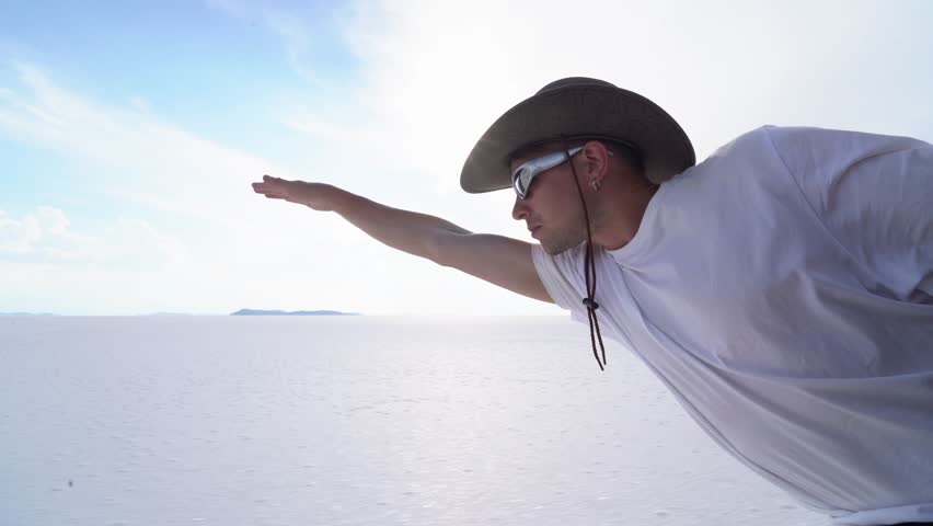 Man Leaning Out of Car Window Pretending to Fly Over Salar de Uyuni Salt Flats – Dynamic Travel Scene in Bolivia