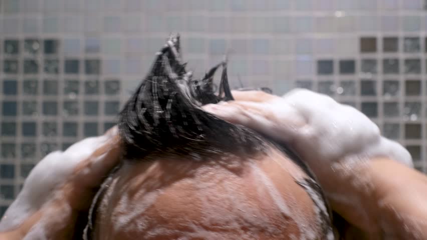 Men's hands wash their hair with shampoo and foam against a gray tile background front view close-up.