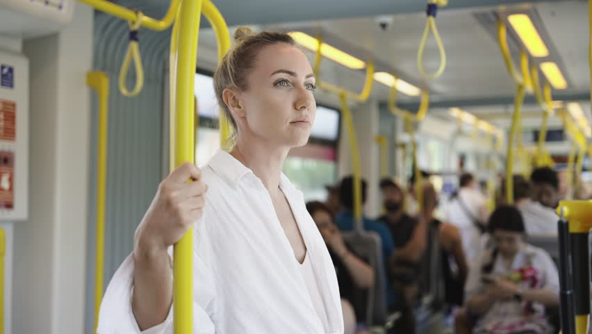 A young woman in a white shirt stands inside a modern city tram, surrounded by other passengers. Showcases comfortable and safe urban public transportation with contemporary design