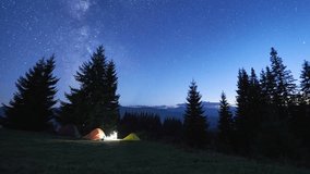 Night camping in mountains. Amidst forested mountain landscape, two tents glow warmly beside campfire under brilliant, star-filled sky. Silhouettes of tourists resting at campsite under Milky Way. - Powered by Shutterstock - Get 15% off with code: PIKWIZARD15