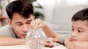 Asian father and son lie down on floor teaching kids for saving money put coins in piggy bank, parenthood lifestyles activities at home, dad spend time with son explain the utility of keeping planning - Powered by Shutterstock - Get 15% off with code: PIKWIZARD15