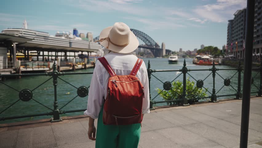 A female tourist stands in Sydney s city center with the iconic Harbour Bridge and sparkling bay as her backdrop. Smiling near the ferry wharf, she embodies summer joy in Australia