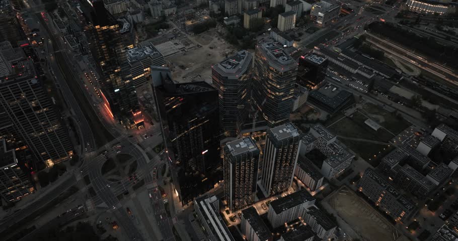 Aerial view of Warsaw in Poland at night featuring illuminated skyscrapers, city traffic, and modern urban landscape.