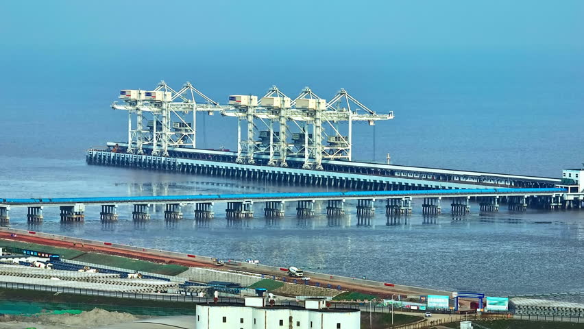 Aerial shot of large cargo cranes on container terminal pier at maritime port by the sea. Global trade logistics and transportation background.