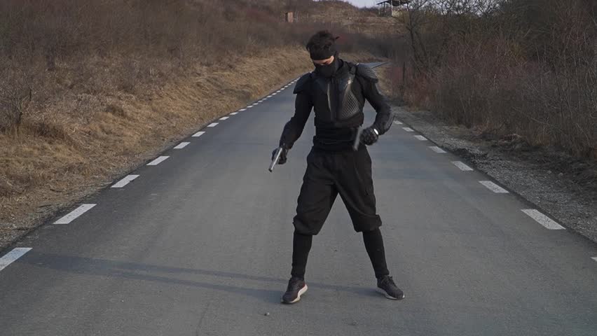 A dynamic shot of a masked ninja with two pistol guns in a combat stance on an empty road. Perfect for action scenes, martial arts content, and cinematic projects.