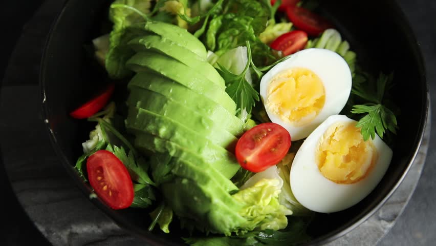 Salad avocado, boiled egg, tomato, green leaf lettuce, vegetable dish fresh delicious gourmet food background on the table rustic food top view copy space
