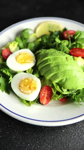 Salad avocado, boiled egg, tomato, green leaf lettuce, vegetable dish fresh delicious gourmet food background on the table rustic food top view copy space