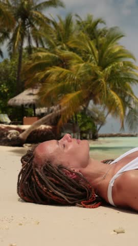 woman with braided hair lies down on soft sandy beach under palm trees, eyes closed enjoying sun and relaxation, tropical paradise in maldives, summer vacation, island retreat