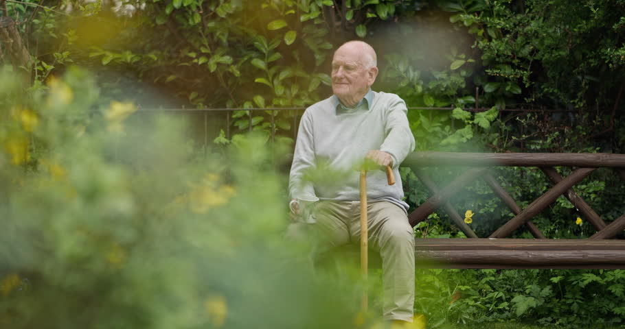 Happy senior man, coffee and park bench in garden for morning, relax or break at retirement home. Calm elderly male person drinking tea in mug or cup sitting with kane on outdoor chair in nature