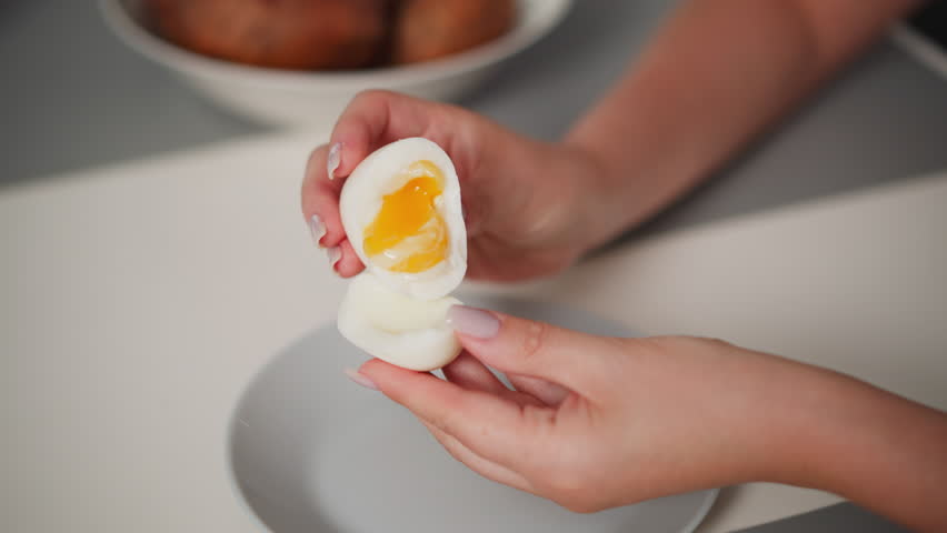 Close up of person holding soft-boiled egg with runny yolk partially turned into other half of white shell over plate, showing texture and gentle handling of fragile egg during food preparation