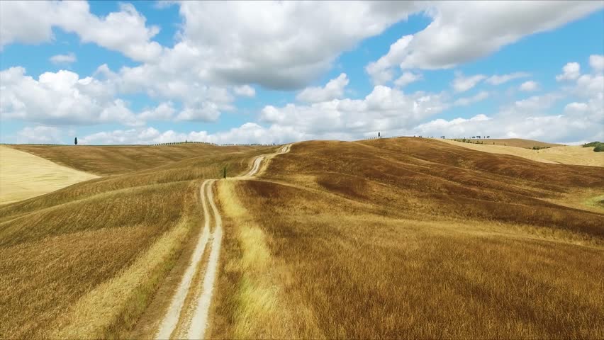 Aerial Drone View Winding Dirt Road Through Dry Golden Rolling Hills Iconic Tuscany Landscape Crete Senesi Italy Blue Sky with Clouds Summer Day Panorama
