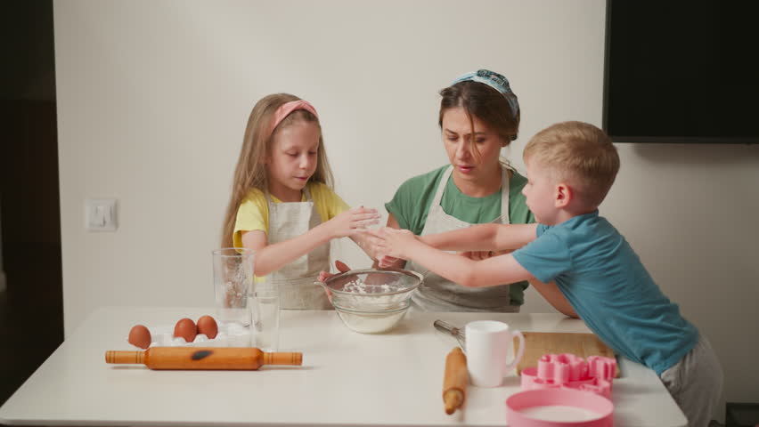 kids playfully dusting flour from hands while baking, causing light mess and laughter as aunt pulls back slightly with surprised expression, showing fun and chaos in family kitchen activity
