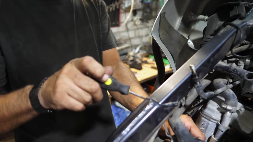 Arms of professional mechanic repairing detail of motorcycle at workplace. Male hands of repairer fixing moto engine at workshop. Adult repairman mending vehicle motor at garage. Slow motion