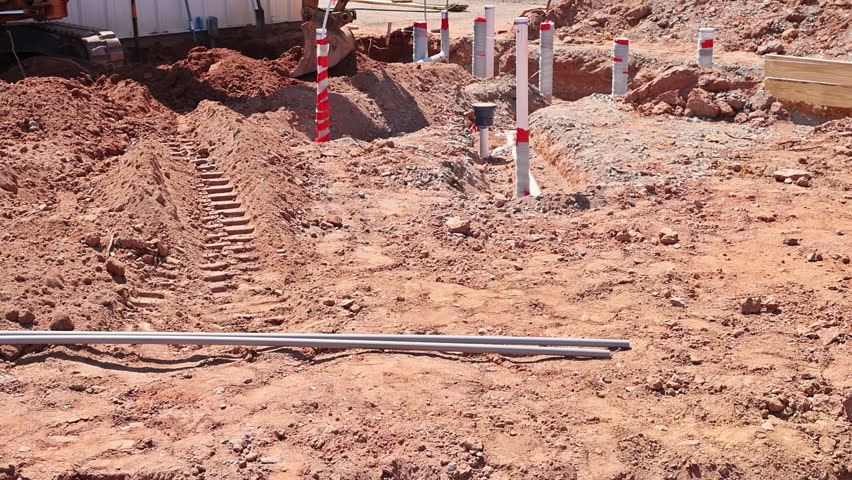 Groundwork for new structure is in progress with soil disturbed markers laid out plumbing pvc pipes