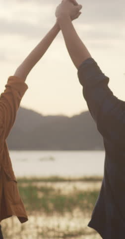 Vertical Screen : Young asia campers couple stand raised arms at campsite near beach. Happy male female traveler success and fun sunset in evening. Outdoor activity, adventure travel holiday vacation.