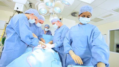 Multi ethnic surgical team in protective clothing performing surgery hospital operating theatre