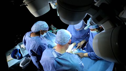 Overhead view multi ethnic surgical team in protective clothing performing surgery hospital operating theatre