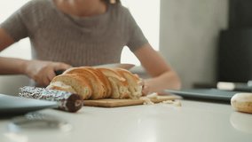 Close up of baker slicing loaf of bread with knife on wooden board focus on serrated blade cutting through crust into even slices with crumbs falling on white table under soft window light in kitchen - Powered by Shutterstock - Get 15% off with code: PIKWIZARD15