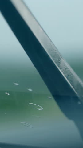 exciting close view black wipers clean raindrops from wet car windshield against blurred driving car