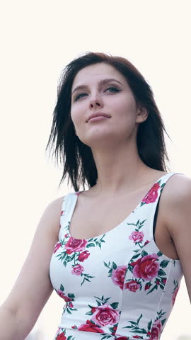 close round motion young pretty woman in dress with flower images fixes hair against huge gray building