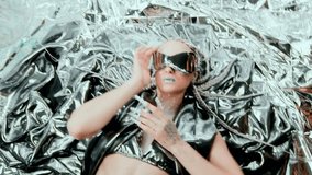 Portrait of a futuristic model lying on chrome foil, wearing a silver outfit and visor. Her glitter lips and pearl nails move expressively, enhancing this stylish sci-fi fantasy with graceful motion. - Powered by Shutterstock - Get 15% off with code: PIKWIZARD15