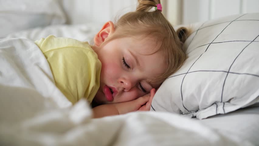 Peaceful adorable baby sleeping on a bed at home. Slumbering little child. Two years old girl sleeps peaceful at domestic room interior background. Serene dream. Cute face close up. Deep kid slumber
