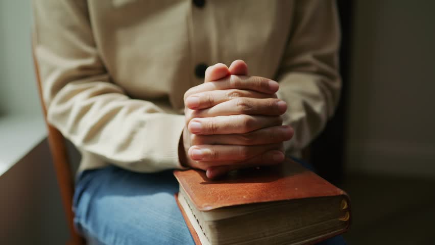 Close-up of a person holding open hands above an open Bible, symbolizing prayer, faith, humility, and spiritual surrender in peaceful reflection.