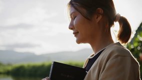 Peaceful young woman smiles with eyes closed, holding a Bible close to her chest in nature, symbolizing faith, hope, and gratitude. - Powered by Shutterstock - Get 15% off with code: PIKWIZARD15