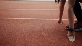 A determined young woman in athletic attire crouches in starting position on an outdoor track, demonstrating focus, strength, and competitive spirit before a race. - Powered by Shutterstock - Get 15% off with code: PIKWIZARD15