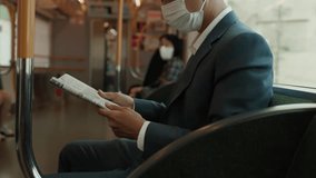 Young businessman in suit and mask reads a newspaper while sitting on a subway train, symbolizing urban commuting, information update, and health safety. - Powered by Shutterstock - Get 15% off with code: PIKWIZARD15