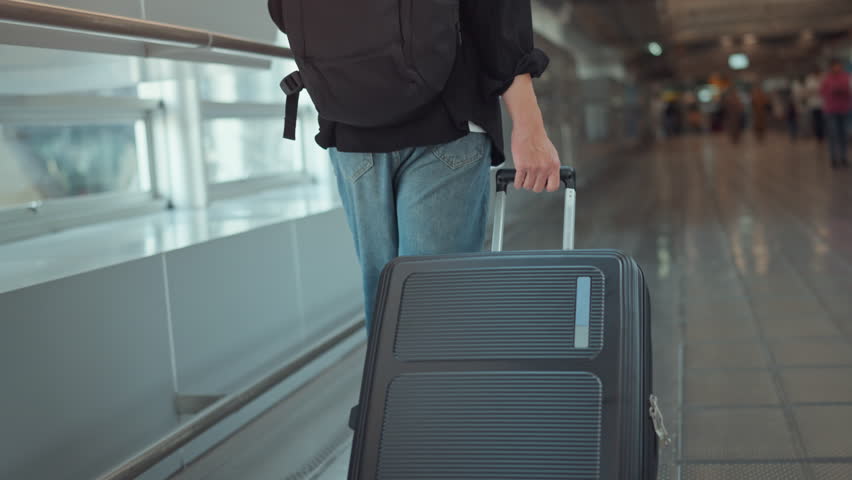 Rear view - Male traveler walking with luggage or suitcase at the modern airport terminal, man on way to flight boarding gate, Ready for travel or vacation journey.