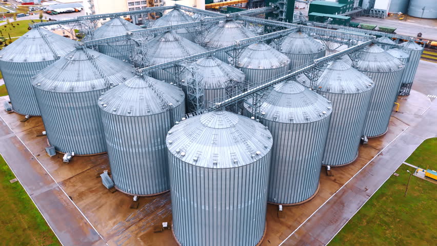 Approaching the rows of metal tanks for grain storage. Elevators at the modern agricultural enterprise. Aerial view.