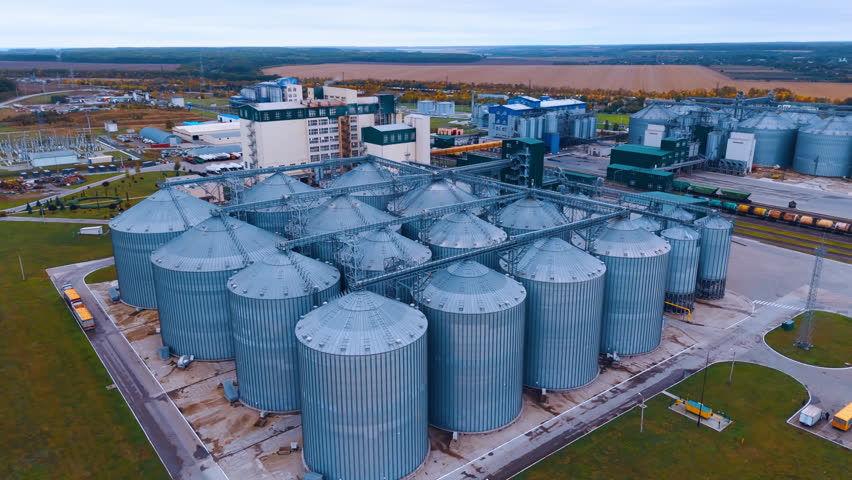 Metal silos on agro-processing and manufacturing plant for processing, drying, cleaning and storage of agricultural products. Aerial perspective on the enterprise in the countryside.