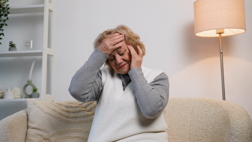 Elderly woman suffering from headache and facial pain at home