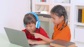 Two young asian girls collaborating on a laptop for online education, wearing headphones and glasses, with books stacked nearby, embodying remote learning and teamwork - Powered by Shutterstock - Get 15% off with code: PIKWIZARD15