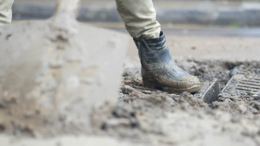 Construction worker digging in muddy ground at city site