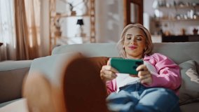 Relaxing girl viewing media content lying on comfy couch. Happy woman watching film on digital device reclining soft sofa. Joyful blonde reading social posts on mobile phone feeling relaxed at weekend - Powered by Shutterstock - Get 15% off with code: PIKWIZARD15