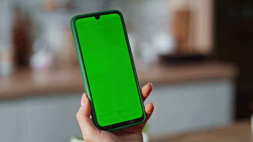 Woman hand scrolling green phone screen indoor closeup. Unknown businesswoman using chromakey smartphone checking social media in apartment. Unrecognized lady holding mockup cellphone reading news 