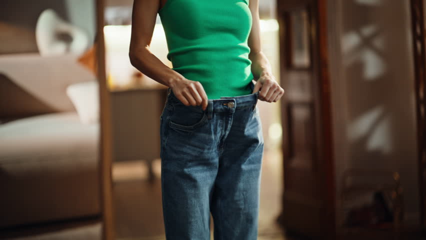 Slim figure trying old jeans closeup. Happy joyful girl enjoying weight loss dieting results. Attractive beautiful woman checking slimming progress looking mirror reflection. Well being motivation 