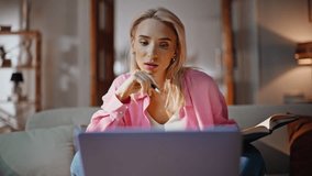 Attentive learner studying at virtual class noting copybook on couch at home interior. Intelligent woman thinking response listening teacher at laptop call in bright living room. Girl writing notebook - Powered by Shutterstock - Get 15% off with code: PIKWIZARD15