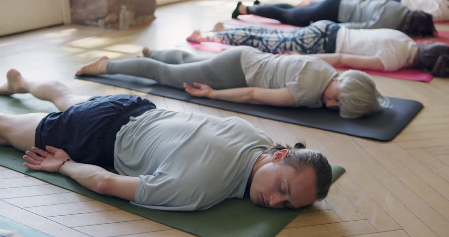 Corpse pose, relax and people in yoga class rest on mat in meditation for holistic, zen or wellness exercise. Group, stretching or lying on the floor and ground in gym with calm breathing practice