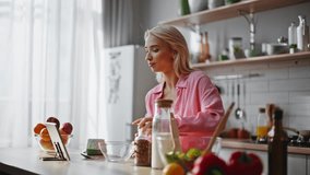 Woman using tablet in kitchen cooking breakfast at morning. Blonde girl looking video recipe on pad computer preparing meal with healthy ingredients. Lady watching gadget at contemporary light cuisine - Powered by Shutterstock - Get 15% off with code: PIKWIZARD15