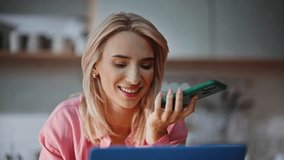 Happy woman recording voice notes at cellphone looking laptop at light home portrait. Cheerful lady enjoying morning talking best friend at cozy kitchen closeup. Relaxed blonde girl conversation  - Powered by Shutterstock - Get 15% off with code: PIKWIZARD15