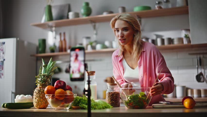 Food vlogger demonstrating fruits to smartphone camera at kitchen closeup. Blonde woman showing healthy organic products recording blog at home. Influencer girl filming culinary tutorial at phone 